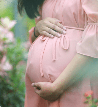 Close up of the belly of a pregnant woman in a pink dress holding her stomach.