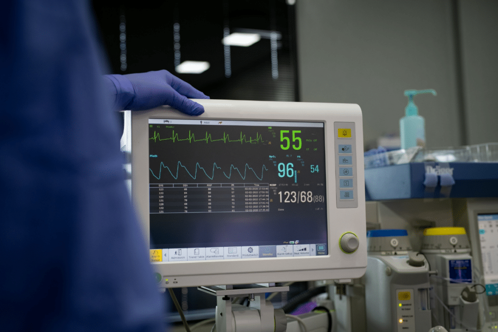 Patient's vitals on a hospital monitor. A surgeon looks like they are standing next to it, with their gloved hand resting on top.