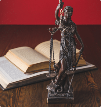 Statue of the lady of justice holding scales. The statue is in front of a book on a desk