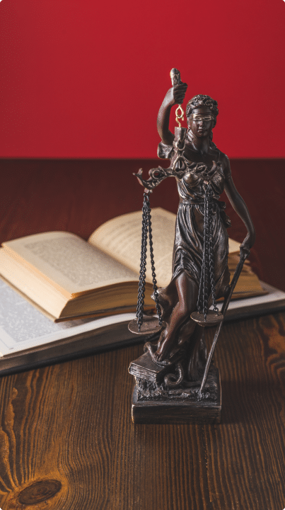 Statue of the lady of justice holding scales. The statue is in front of a book on a desk