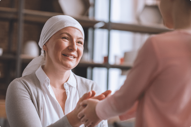 woman with cancer, wearing a headscarf to keep her warm. She is holding hands with a family member